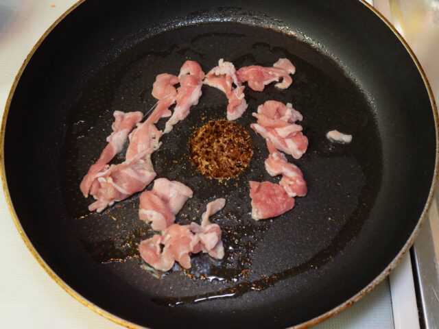 フライパンにサラダ油を熱して、豚こま肉を入れた写真