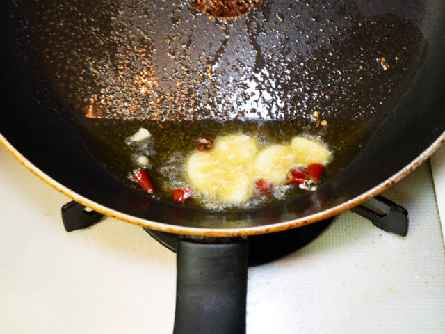 フライパンにオリーブオイル、オイルサーディンの油ニンニク、唐辛子を入れて弱火で加熱する写真