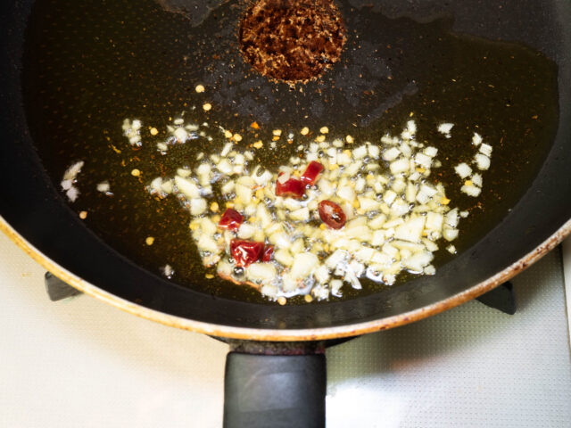 フライパンにオリーブオイル、ニンニク、唐辛子を入れて弱火で加熱する写真