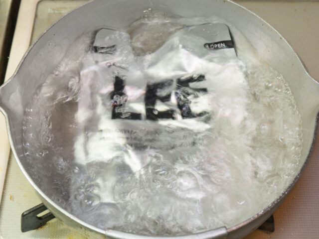 鍋にお湯を沸かし、レトルトカレーを湯煎する写真