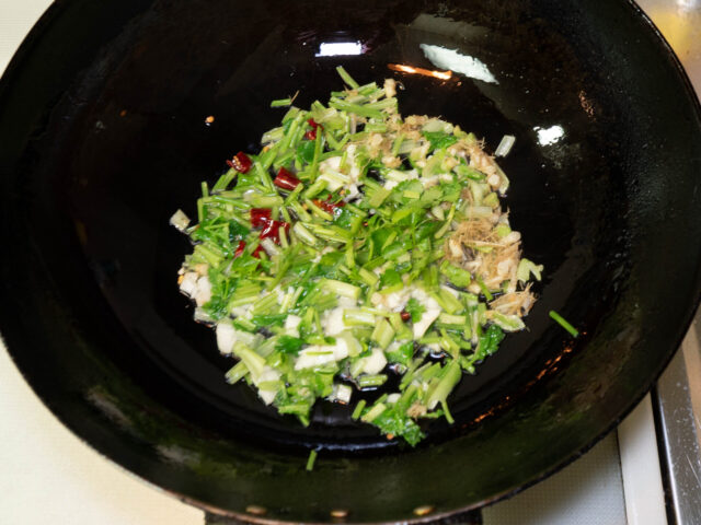 中華鍋にサラダ油を熱して、パクチーの根と茎、ニンニク、唐辛子を炒める写真