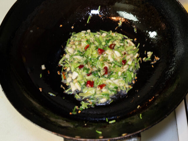 中華鍋にサラダ油を熱して、パクチーの根と茎、ニンニク、唐辛子を炒める写真
