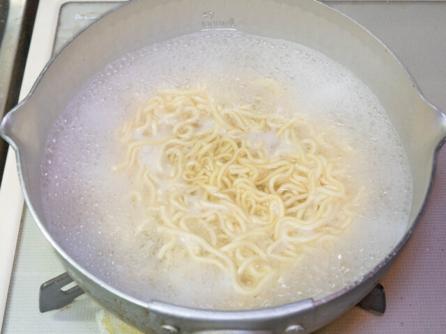 鍋にお湯を沸かし、インスタント麺を茹でる写真