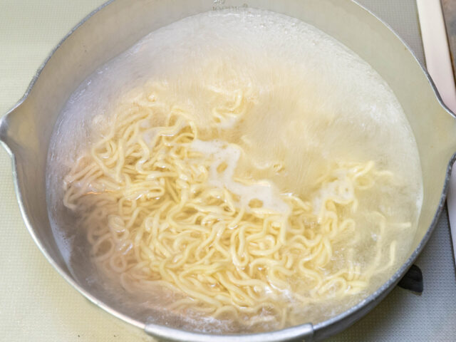鍋にお湯を沸かしてインスタント麺を茹でる写真