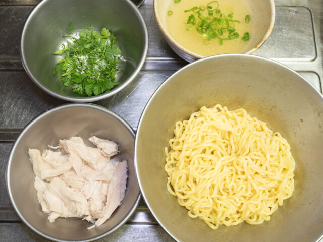 ボウルの中でスープと混ぜた麺、ほぐした茹で鶏、刻んだパクチー、残りのスープにお湯を注いだスープの写真