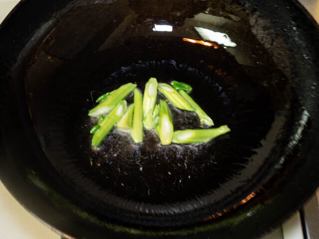 中華鍋にサラダ油を熱して、かき菜の茎を加えた写真