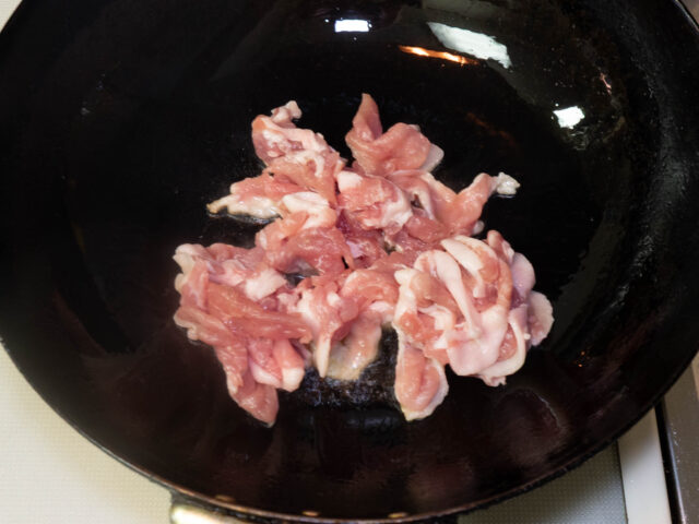 中華鍋にごま油を熱して豚肉を加えた写真