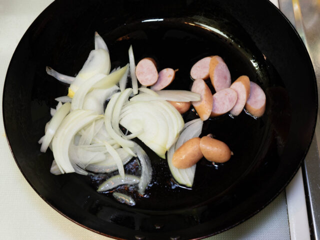 フライパンにサラダ油を熱して、ウィンナーと玉ねぎを加えた写真