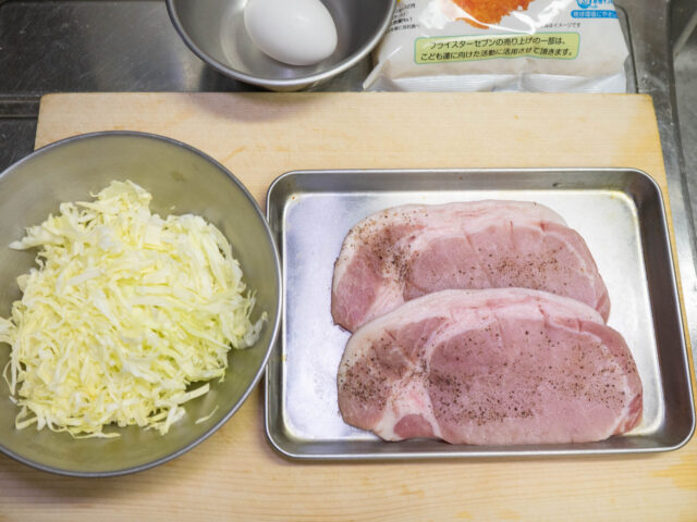 筋切りをして塩と胡椒をまぶした豚肉、千切りにしたキャベツの写真