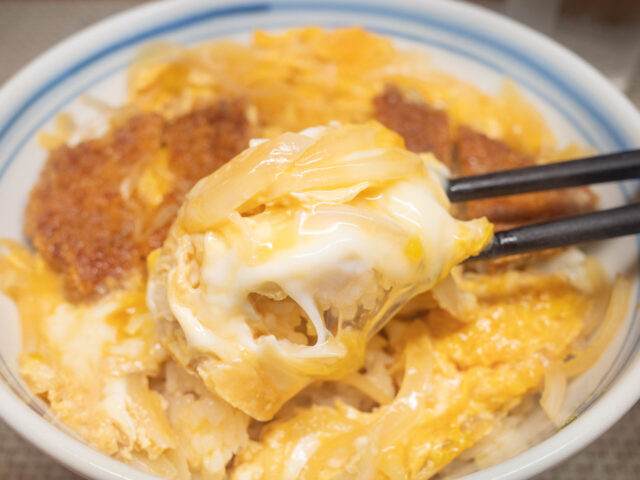 卵でとじた玉ねぎとご飯を箸で持ち上げた写真