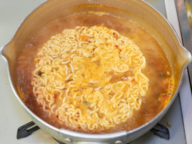鍋にお湯を沸かし、インスタント麺を加えた写真