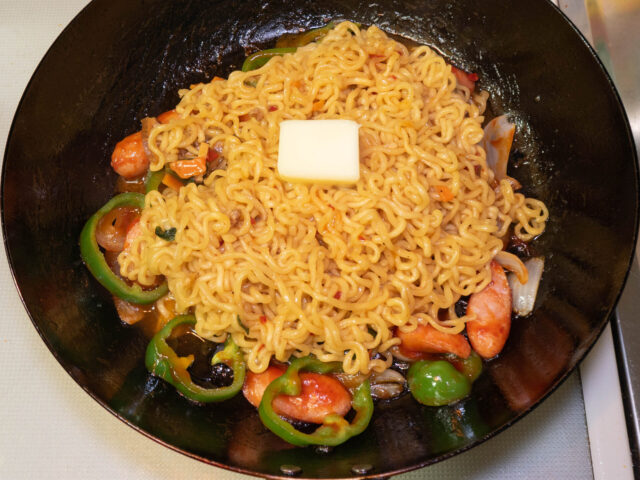 具材を炒めたフライパンに茹でた麺とバターを加えた写真